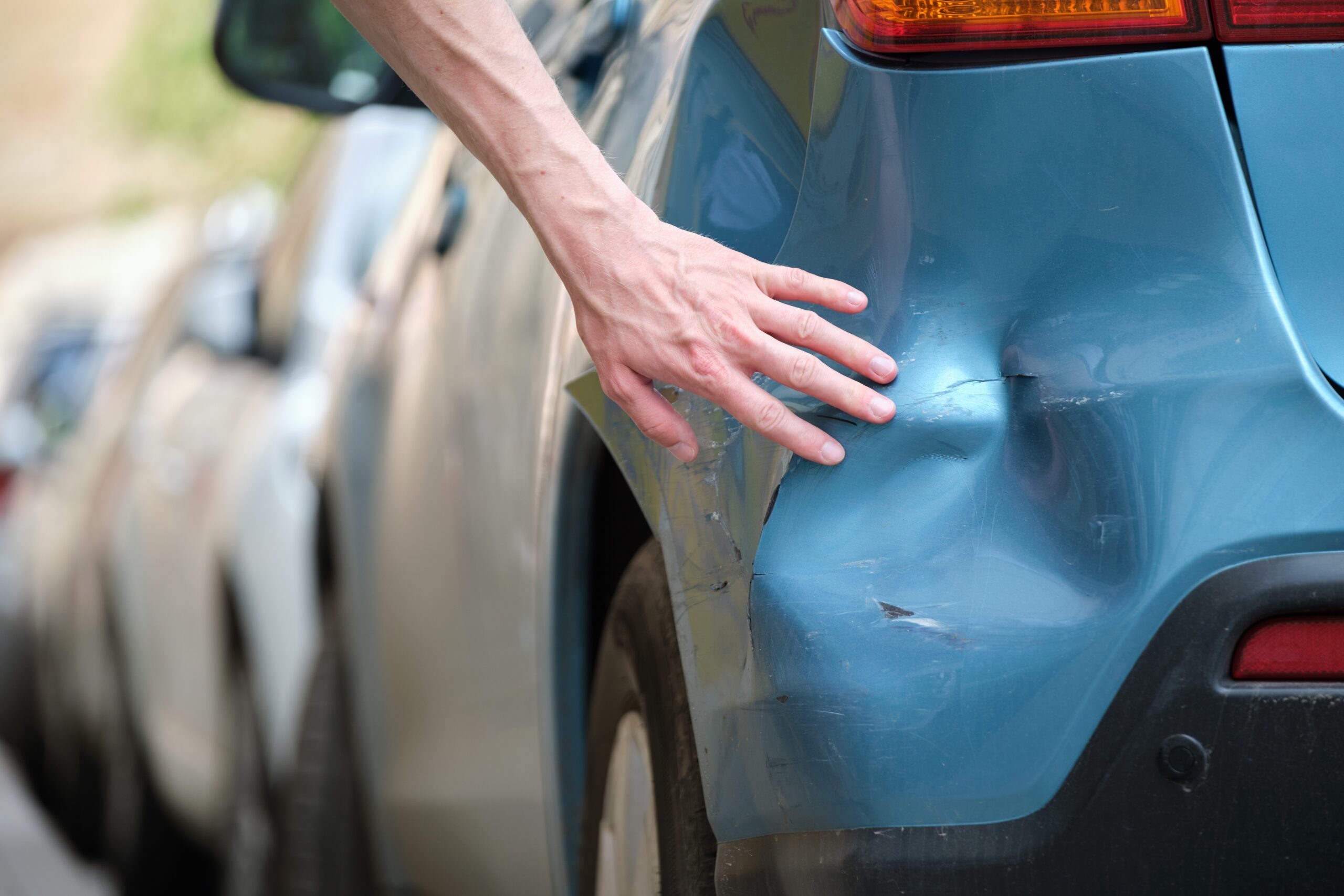 Close-up of a person's hand inspecting a large dent on the rear bumper of a blue car, illustrating hit-and-run Florida legal claims.